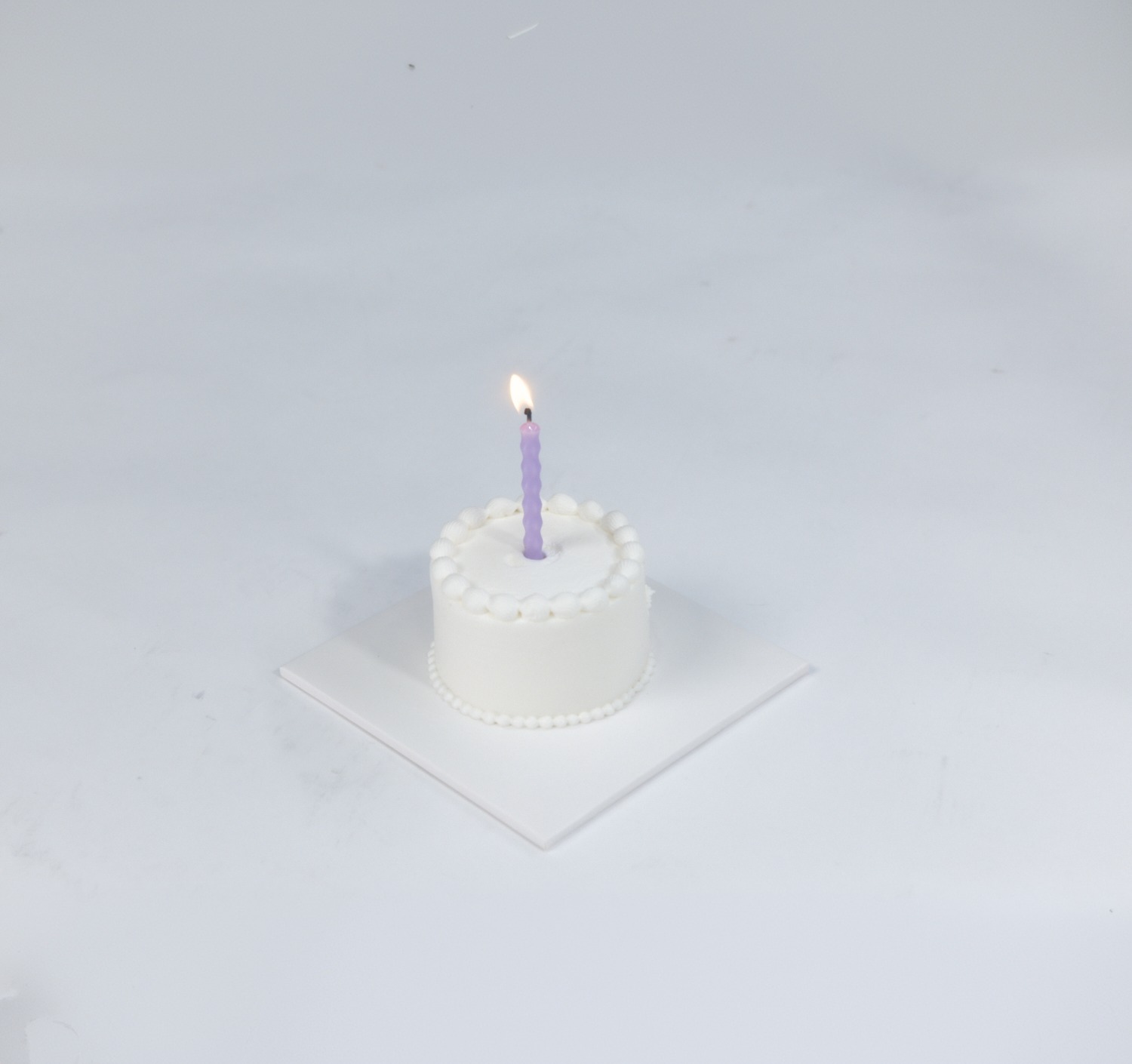 A single white cake with one lit candle
